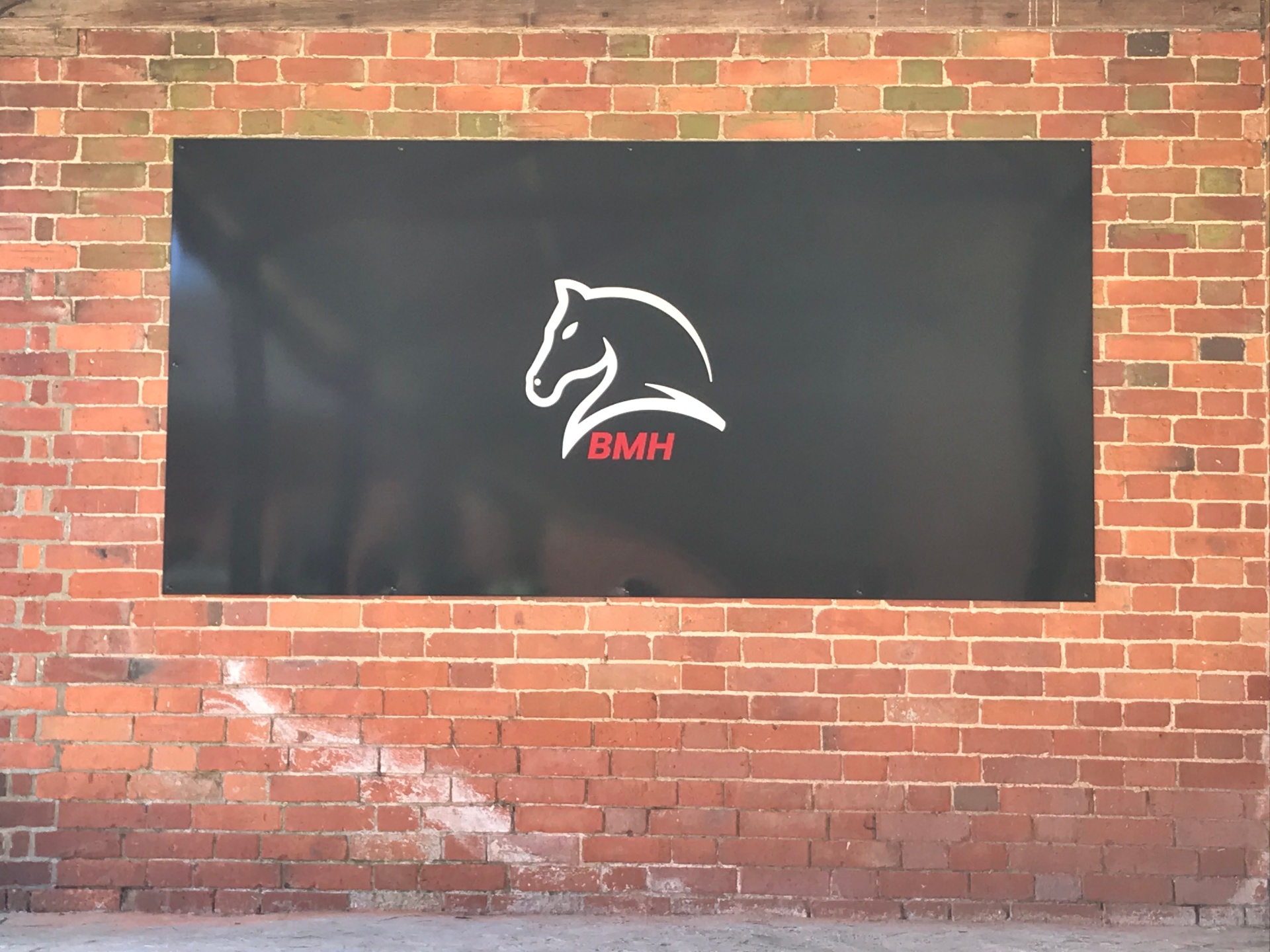 Large BMH branded sign mounted on the brick stable wall